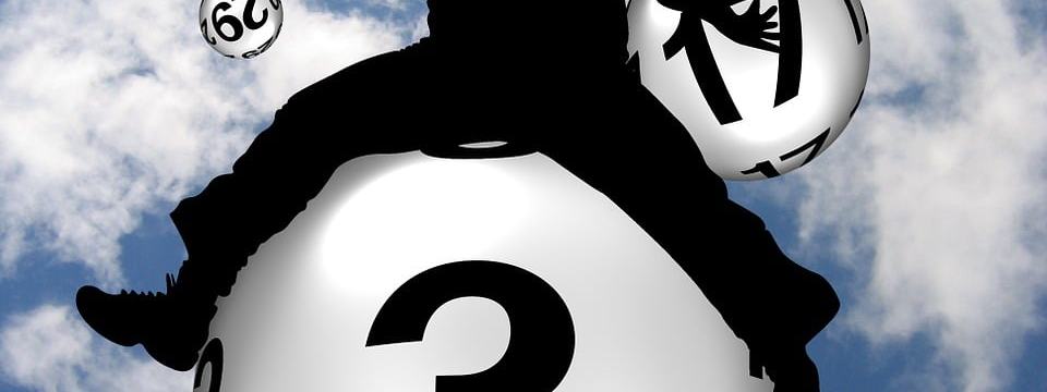 A man flies towards the sky sitting on a Lotto ball with the number 3. Around him are several balls with other numbers.